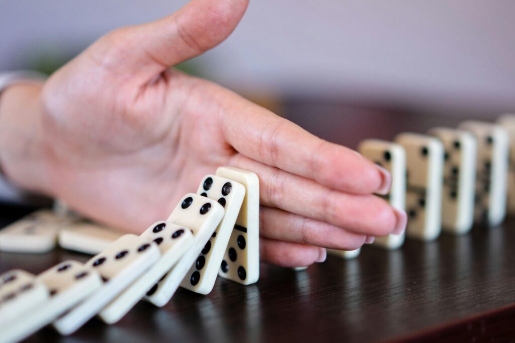 Hand stopping a line of falling dominoes, symbolizing interrupting self-defeating behavior and inner saboteur — inspired by Dorice Horenstein’s teachings.