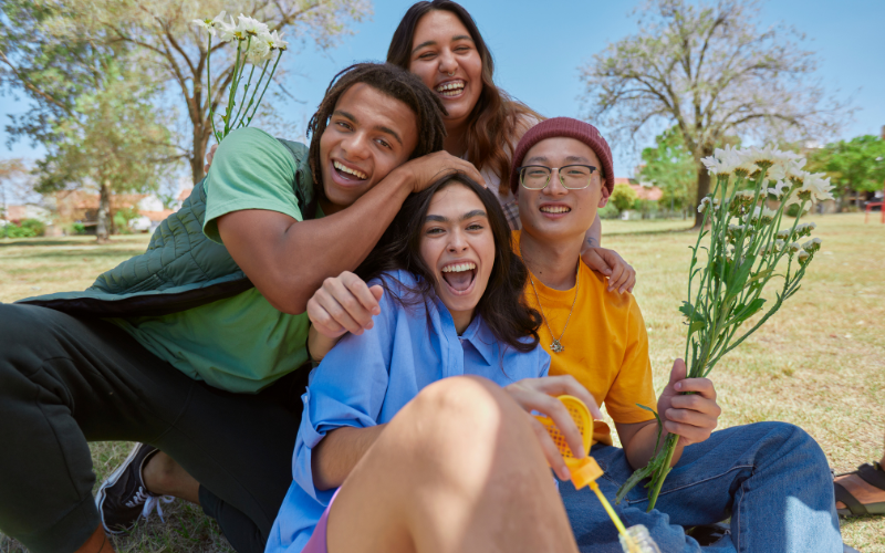 Group of four people sitting on the ground, smiling with authentic connection—showing genuine positivity through joy, groundedness, and emotional well-being.