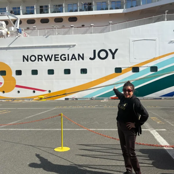 Dorice Horenstein standing on a dock, smiling and pointing proudly at the "Norwegian JOY" ship name to visualize the blog's core message of utilizing joy as a leadership advantage for high-performing, mentally fit teams.