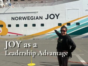 Dorice Horenstein standing on a dock, smiling and pointing proudly at the "Norwegian JOY" ship name to visualize the blog's core message of utilizing joy as a leadership advantage for high-performing, mentally fit teams.