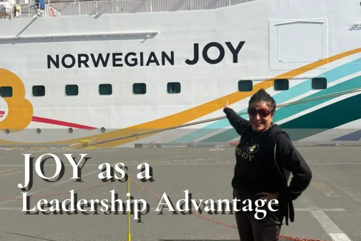 Dorice Horenstein standing on a dock, smiling and pointing proudly at the "Norwegian JOY" ship name to visualize the blog's core message of utilizing joy as a leadership advantage for high-performing, mentally fit teams.